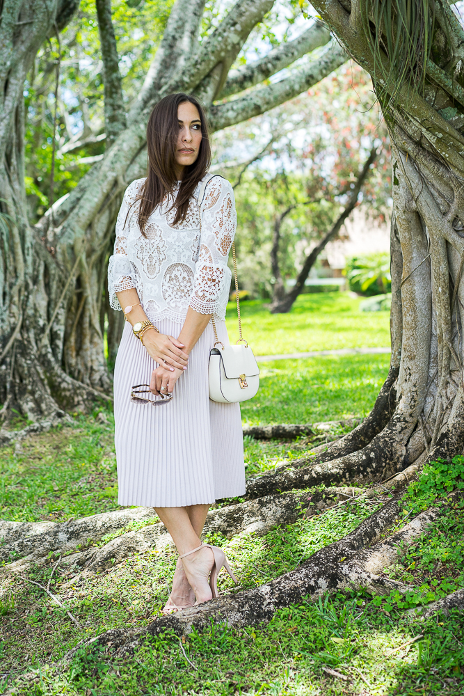 Amanda Champion wearing White lace bell sleeve top, blush pleated skirt and white bag