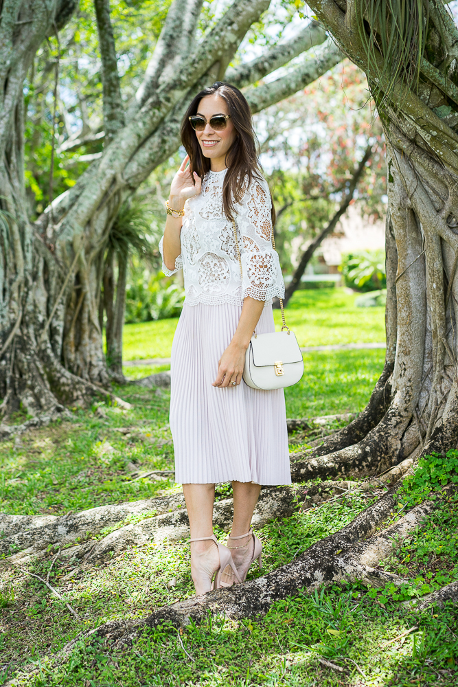 Amanda Champion wearing White lace bell sleeve top and blush pleated skirt