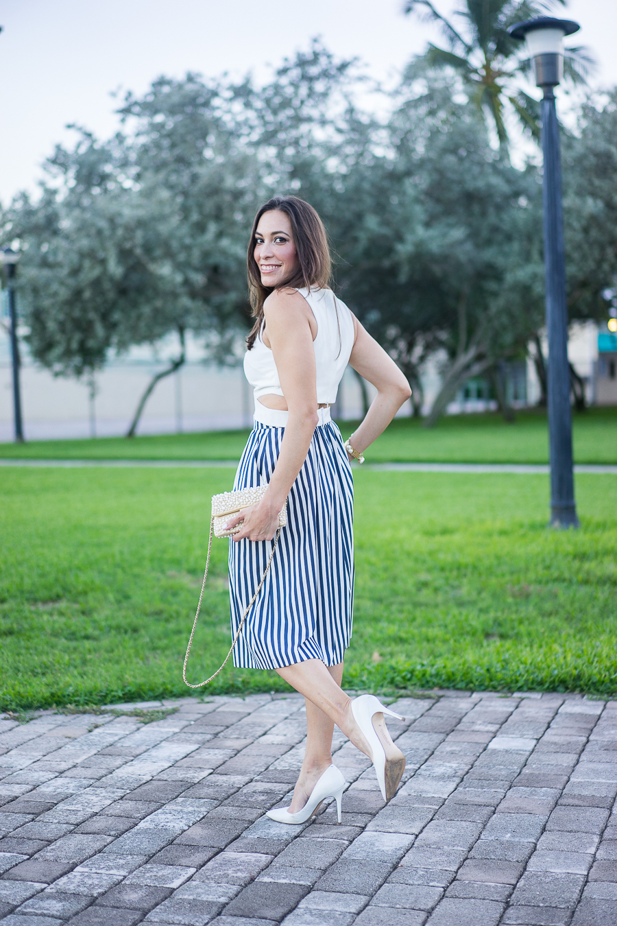 A Glam Lifestyle fashion blogger wearing white crop top with a striped skirt and chanel pearl bag