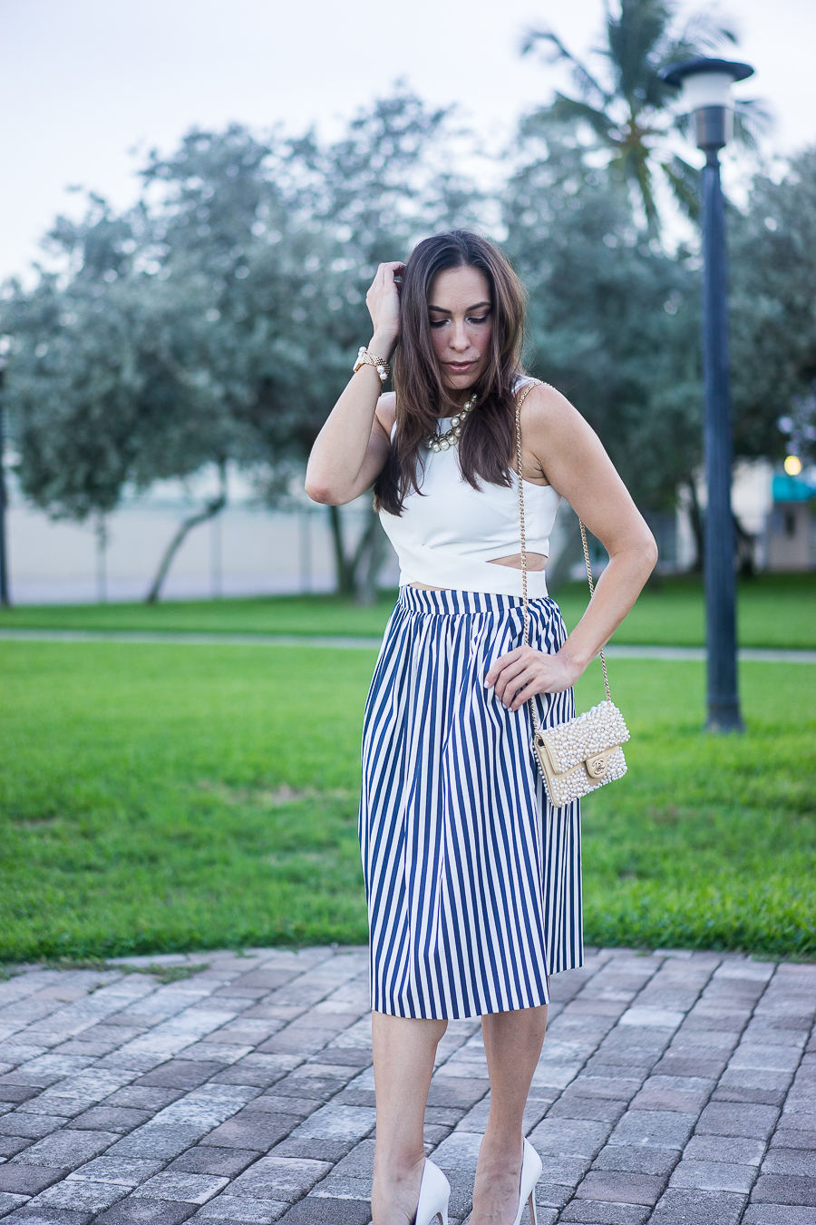 A Glam Lifestyle fashion blogger wearing white crop top with a striped skirt and chanel pearl bag
