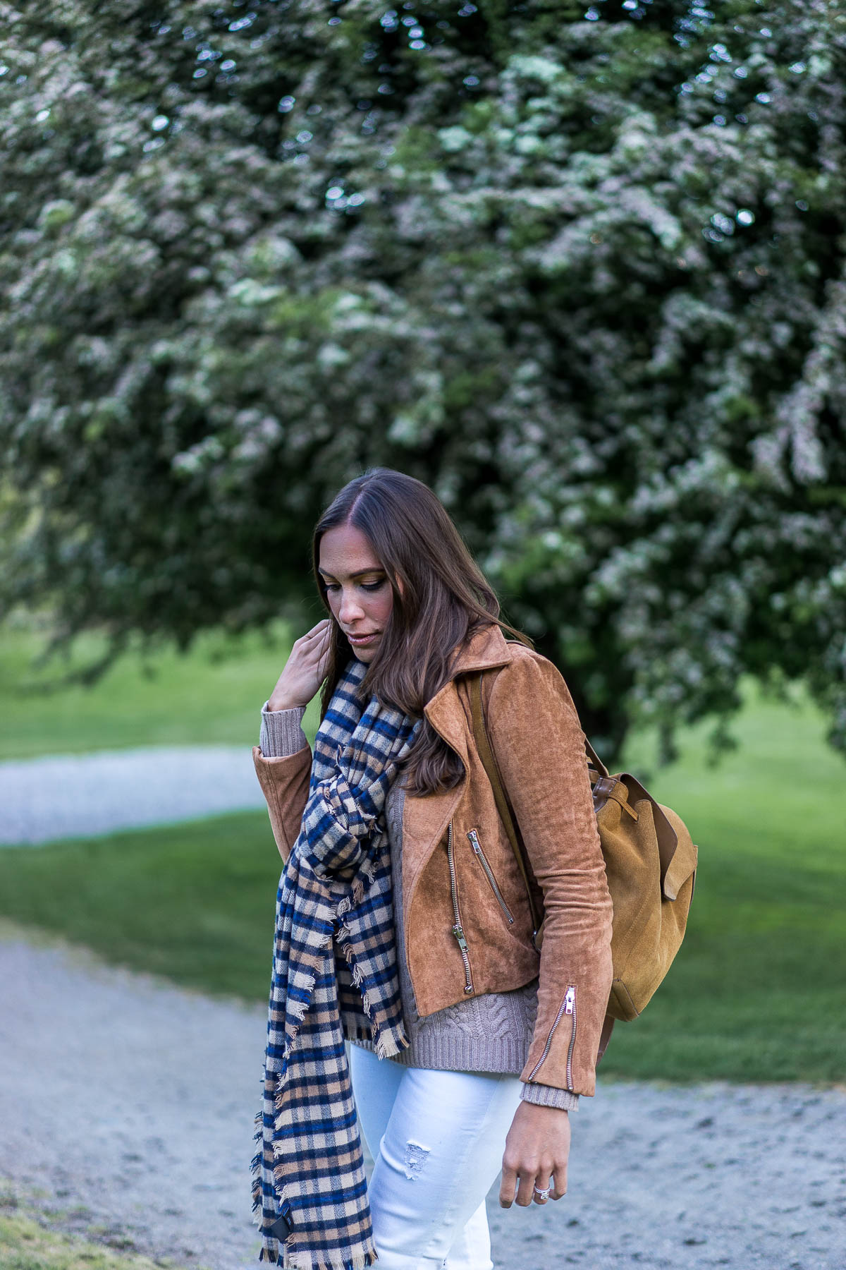 a glam lifestyle fashion blogger wears tan suede moto jacket and long blanket scarf over cold shoulder cable knit sweater with backpack