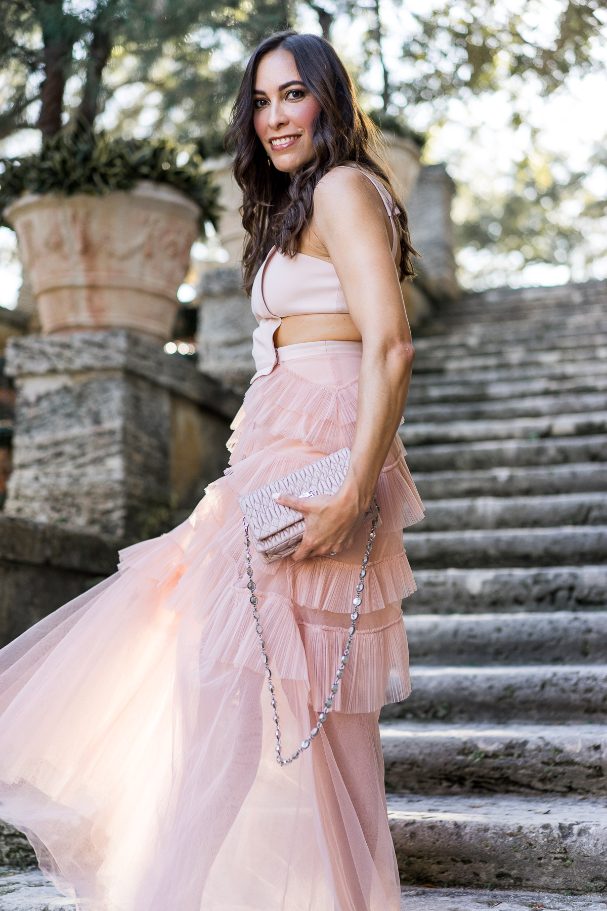 A Glam Lifestyle blogger wears BCBG Avalon blush tulle dress while carrying Miu Miu Nappa Crystal bag at Viscaya Gardens in Miami