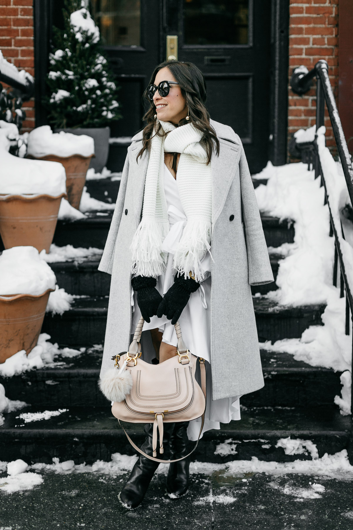 A Glam Lifestyle bloggers wears Carolina Constas high low white shirt dress for NYFW street style while carrying her Chloe Marcie bag and Club Monaco coat and white fringed scarf in Greenwich Village