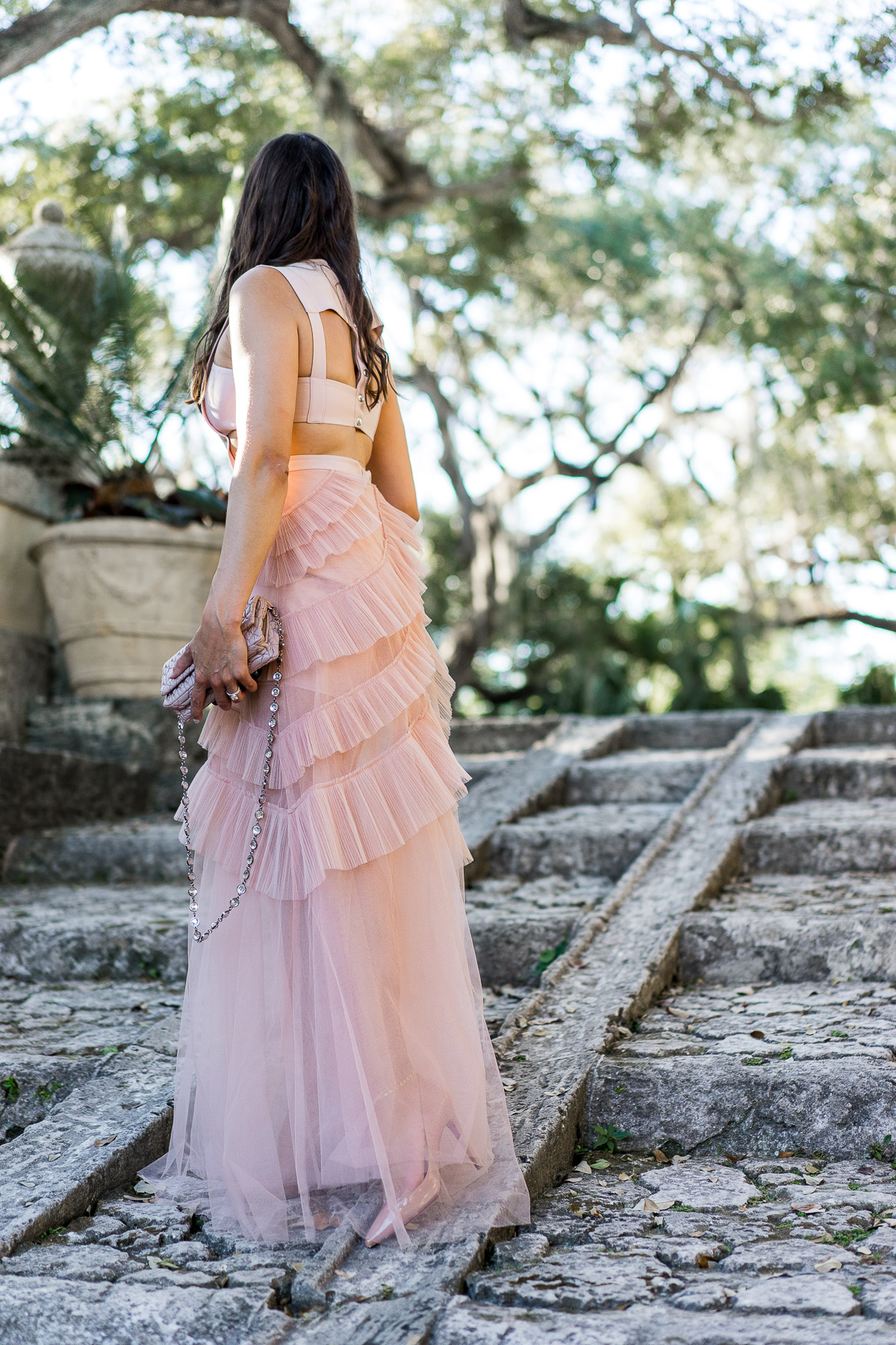 A Glam Lifestyle blogger wears stunning blush tulle dress by BCBG at Viscaya Gardens in Miami with her Miu Miu bag and Louboutin Pigalle pumps