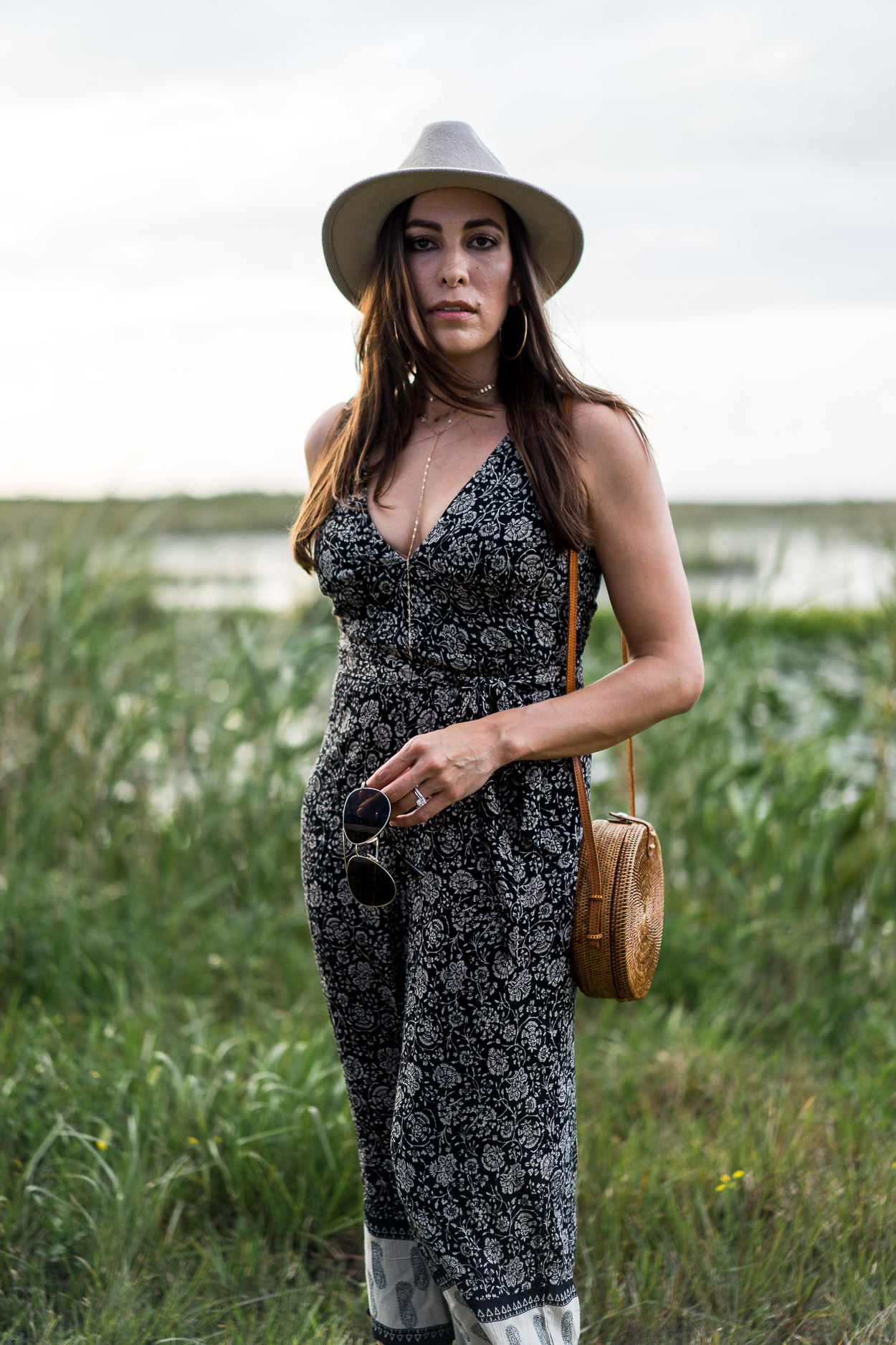 Blogger Amanda of A Glam Lifestyle wears boho style jumpsuit by Amuse Society with Summer style must haves including round basket bag and gold Parpala jewelry