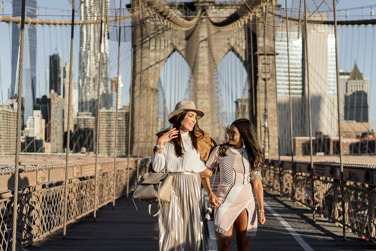 Amanda from A Glam Lifestyle blog styles a metallic pleated skirt with a cream blouse from Aritzia and her Celine belt bag during NYFW with fellow blogger Kelsey Kaplan Fashion