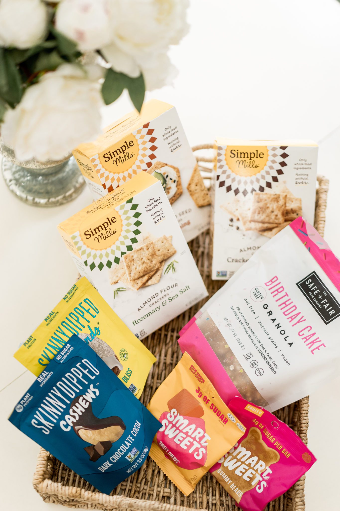 Healthy Snack Ideas for Working From Home by popular Florida lifestyle blog, A Glam Lifestyle: image of Simple Mills crackers, Safe + Fair birthday cake granola, Skinny Dipped Cashews, Skinny Dipped almonds, and Smart Sweets. 